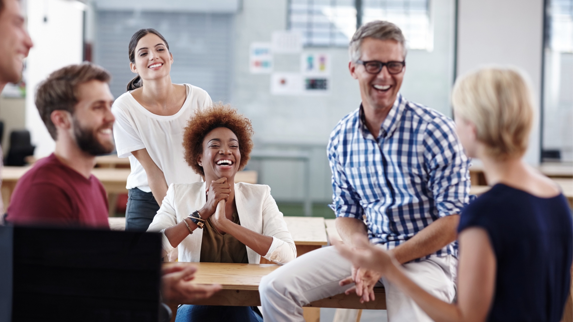 a group of male and female coworkers gathered around some tables, talking and laughing.