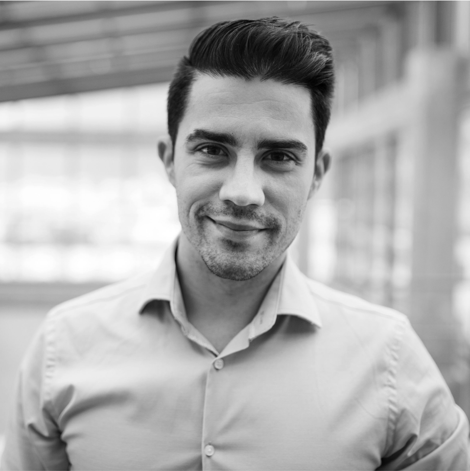 Black and white portrait of a male working professional in a light shirt, smiling slightly, with a blurred office background