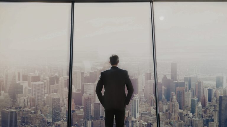 Business man looking out a large window onto the city.