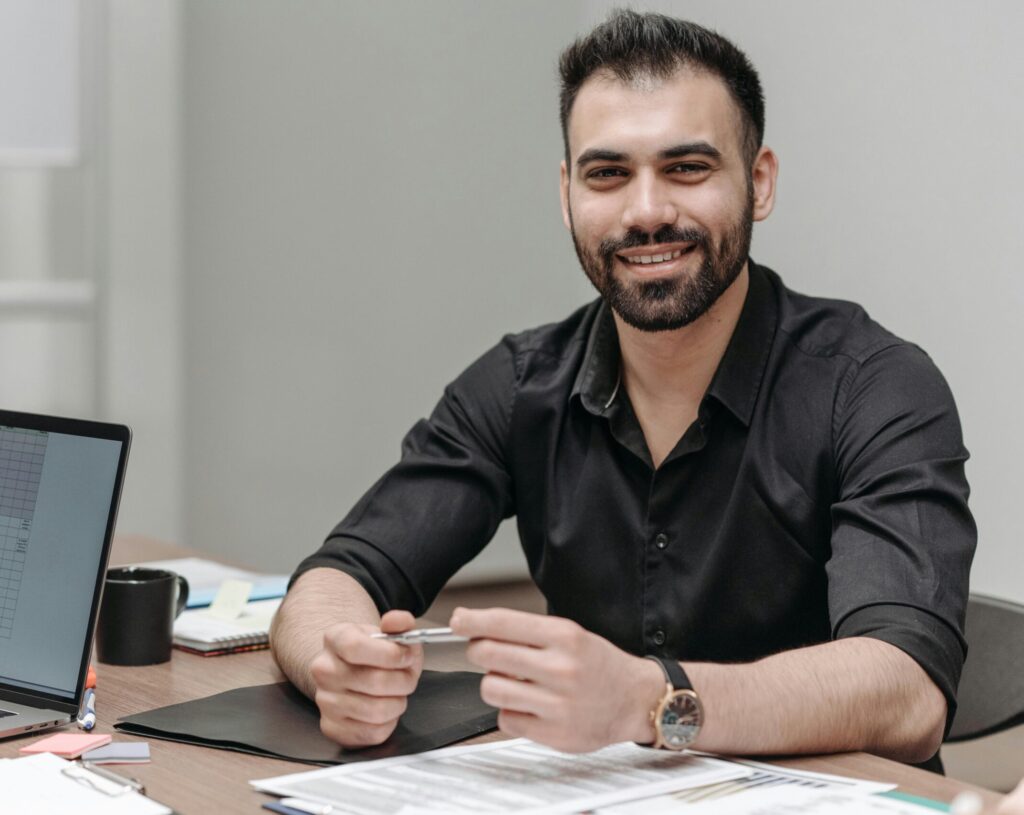 A procurement manager seated at a desk, smiling, with spreadsheets and reports—representing vendor management, purchasing strategy, and supply chain planning.