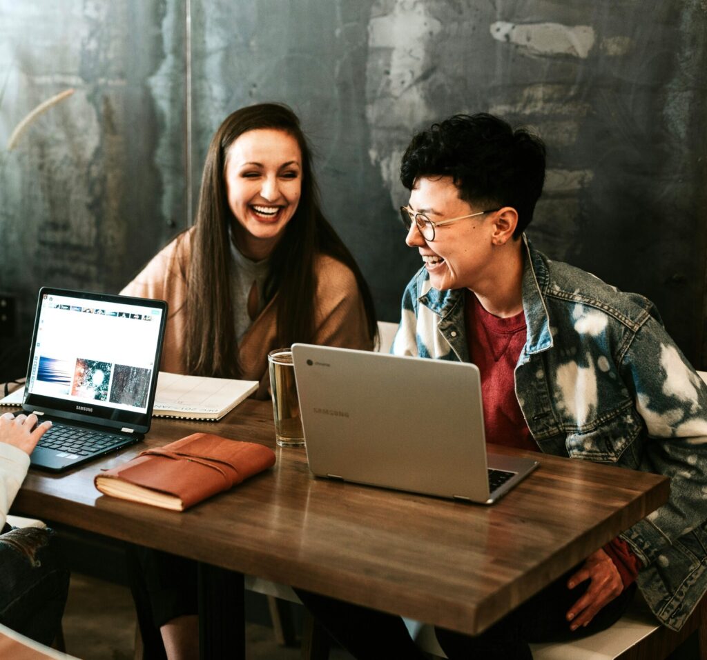 Two professionals collaborating at a table with laptops, sharing ideas and enjoying a positive, productive work environment.