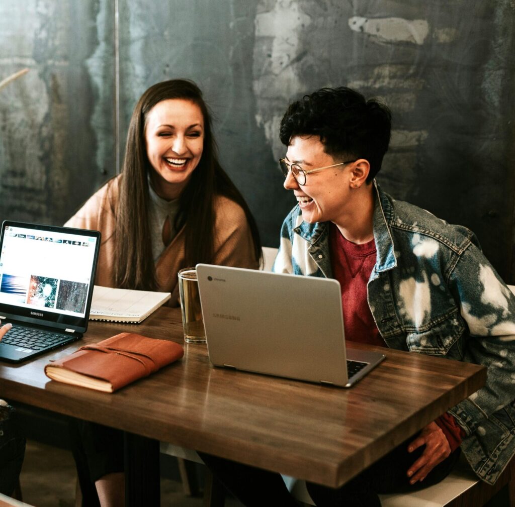 Two professionals collaborating at a table with laptops, sharing ideas and enjoying a positive, productive work environment.