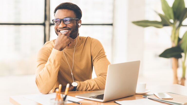 African American Male in a Yellow Sweater Smiling and using Laptop.